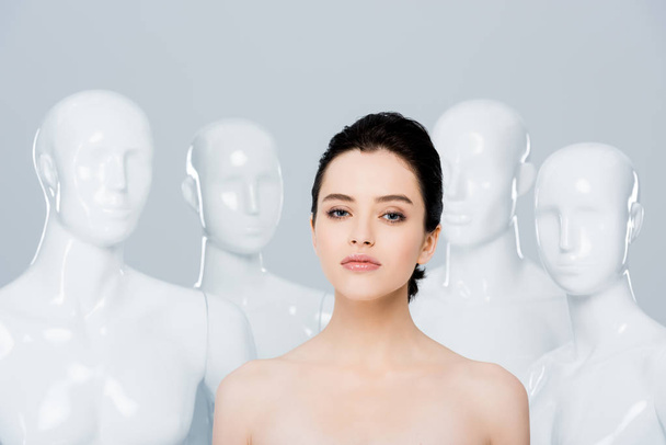 beautiful nude young woman looking at camera near mannequins isolated on grey  - Foto, Bild
