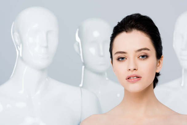 beautiful naked young woman looking at camera near mannequins isolated on grey  - 写真・画像