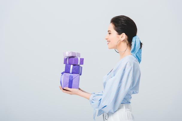 side view of beautiful stylish girl holding gift boxes isolated on grey - Photo, Image