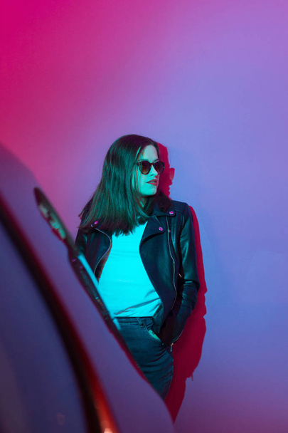 Fashioned girl in leather jacket in dark glasses in pink and blue  neon lights background.  - Foto, Bild