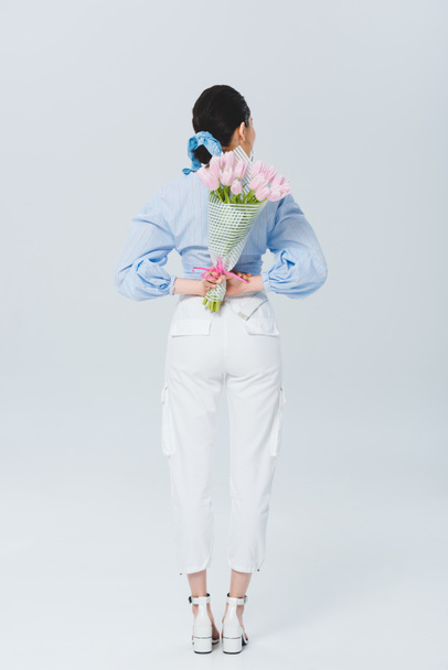 Back view of stylish girl with bouquet of tulips on grey - Foto, afbeelding