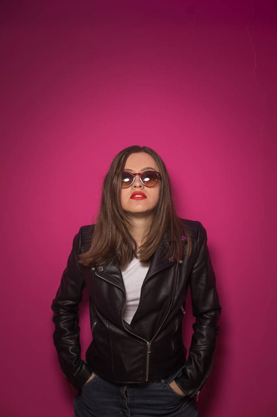 Fashioned girl in leather jacket in dark glasses in pink and blue  neon lights background.  - Φωτογραφία, εικόνα