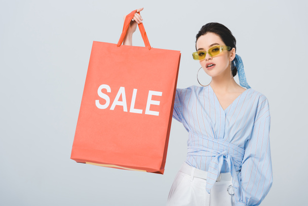 beautiful stylish girl holding shopping bag with sale word isolated on grey - Фото, изображение