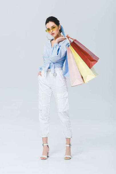 hermosa chica de moda sosteniendo bolsas de compras y mirando a la cámara en gris
 - Foto, imagen