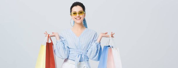 panoramic shot of beautiful stylish girl with shopping bags smiling isolated on grey - Foto, imagen