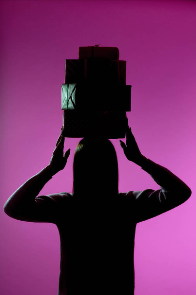 silhouette of a girl with a stack of gift boxes on her head, figure of a woman holding presents, concept of holidays - Foto, immagini