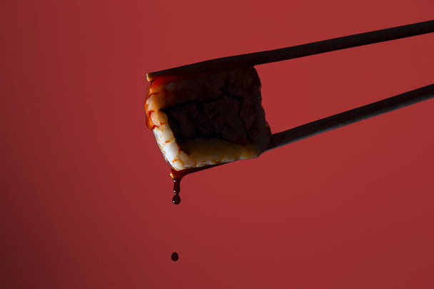 silhouette of succulent roll between chopsticks on a colored background, drops of soy sauce dripping from sushi, food background, Japanese cuisine - Photo, image