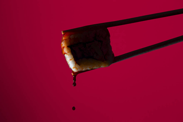 silhouette of succulent roll between chopsticks on a colored background, drops of soy sauce dripping from sushi, food background, Japanese cuisine - Foto, imagen