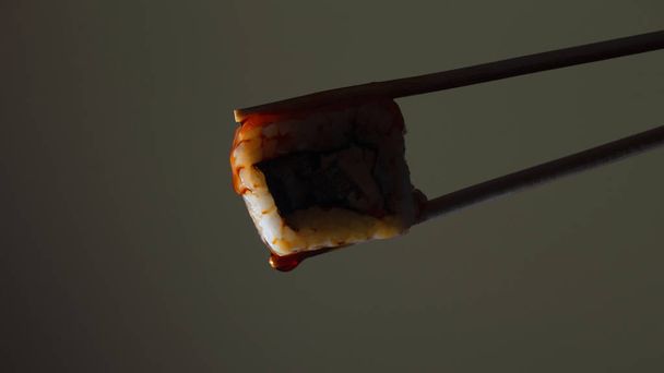silhouette of succulent roll between chopsticks on a colored background, drops of soy sauce dripping from sushi, food background, Japanese cuisine - Photo, Image