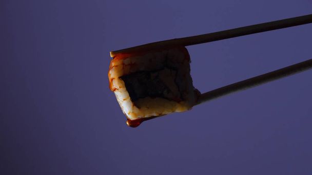 silhouette of succulent roll between chopsticks on a colored background, drops of soy sauce dripping from sushi, food background, Japanese cuisine - Foto, Imagem