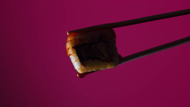 silhouette of succulent roll between chopsticks on a colored background, drops of soy sauce dripping from sushi, food background, Japanese cuisine - Valokuva, kuva