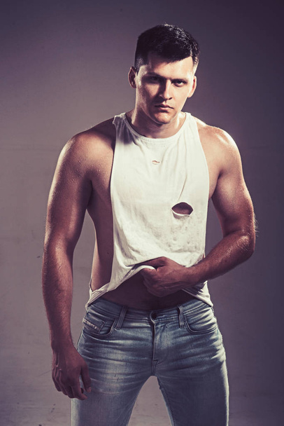 Man in sexy tank top and jeans on grey background. Man with muscular hands with biceps and triceps - Foto, immagini