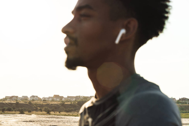 Handsome young african strong sports man listening music with earphones outdoors. - Fotó, kép
