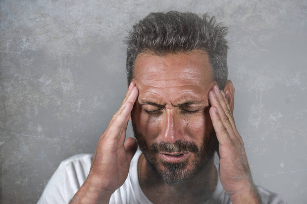 Nahaufnahme dramatisches Porträt eines jungen attraktiven ängstlichen und depressiven Mannes mit schmerzenden Händen auf dem Kopf, der unter Kopfschmerzen und Migräne und Depressionen leidet - Foto, Bild
