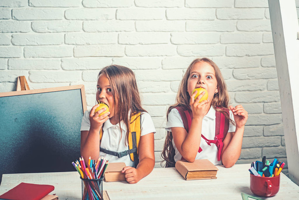 School time of girls. Friendship of small sisters in classroom at knowledge day. Happy school kids at lesson in september 1. Back to school and home schooling. Little girls eat apple at lunch break - Fotografie, Obrázek