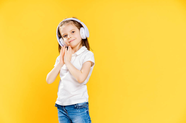 Girl listening to music in wireless headphones on yellow background . Dancing girl. Happy small girl dancing to music. Cute child enjoying happy dance music. - Foto, Imagen