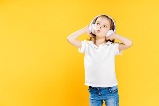 Girl listening to music in wireless headphones on yellow background . Dancing girl. Happy small girl dancing to music. Cute child enjoying happy dance music. - Photo, image