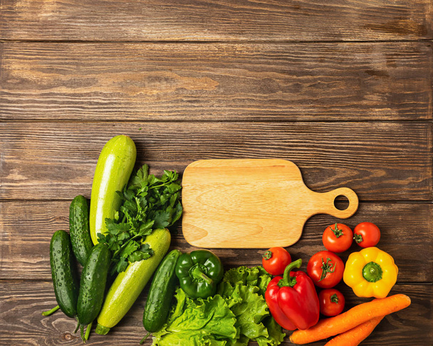 Fresh vegetables of different colors cutting board wooden background. Vegetarianism and healthy nutrition. Flat layout. - Fotó, kép