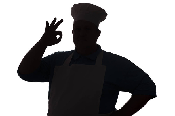 silhouet van een gelukkige chef-kok op een witte geïsoleerde achtergrond, mannelijke hand toont OK - Foto, afbeelding
