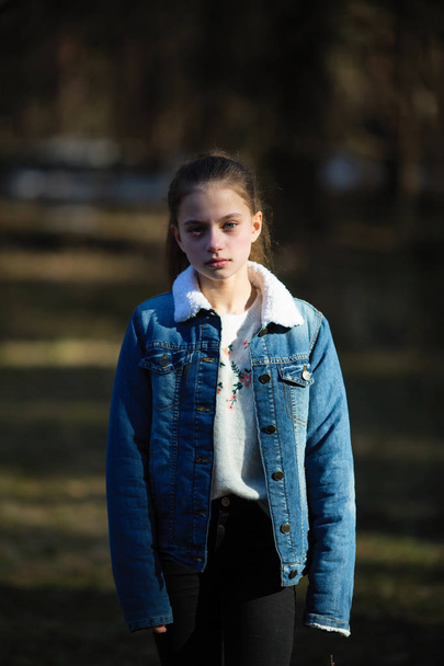 Retrato de una dulce niña de doce años con chaqueta de mezclilla, sesión de fotos en el parque de primavera
. - Foto, imagen