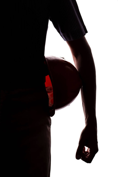 σιλουέτα ενός άνδρα με προστατευτικό κράνος κάτω από το μπράτσο του σε ένα λευκό απομονωμένο φόντο, η έννοια της μηχανικής και της κατασκευής - Φωτογραφία, εικόνα