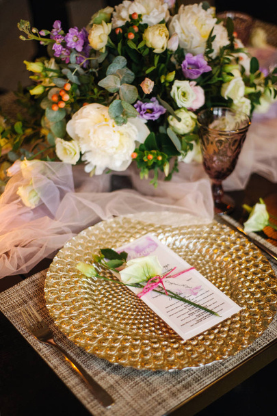 Table setting in golden style with natural flowers at the restaurant. Wedding bouquet, fabric decoration on table, inviting cards, glasses and cutlery - Photo, Image