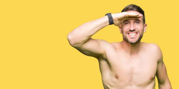 Handsome shirtless man showing nude chest very happy and smiling looking far away with hand over head. Searching concept. - Photo, Image