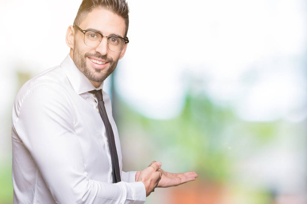 Young handsome business man wearing glasses over isolated background Inviting to enter smiling natural with open hand - Photo, Image
