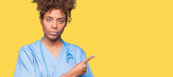 Молодий афроамериканець лікар жінка над ізольованих тло наведення рука пальцем у бік показ реклами, серйозний і спокійний обличчя - Фото, зображення