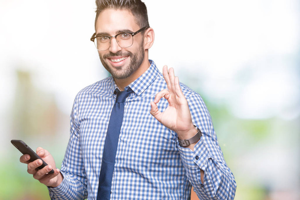 Fiatal üzletember használ smartphone, mint ok jel ujjaival, kiváló szimbólum izolált háttérben - Fotó, kép