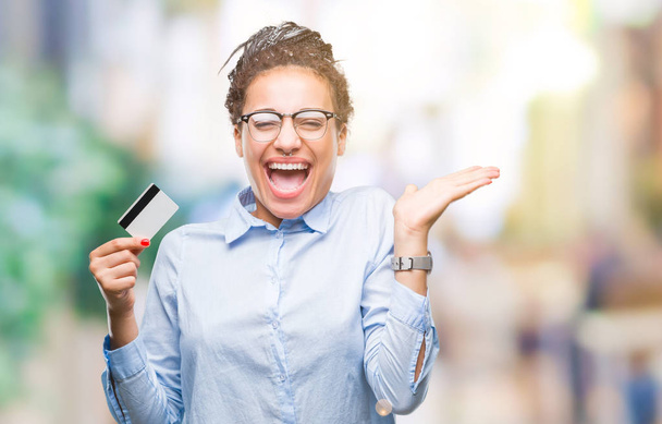 Young african american girl holding credit card over isolated background very happy and excited, winner expression celebrating victory screaming with big smile and raised hands - Foto, immagini