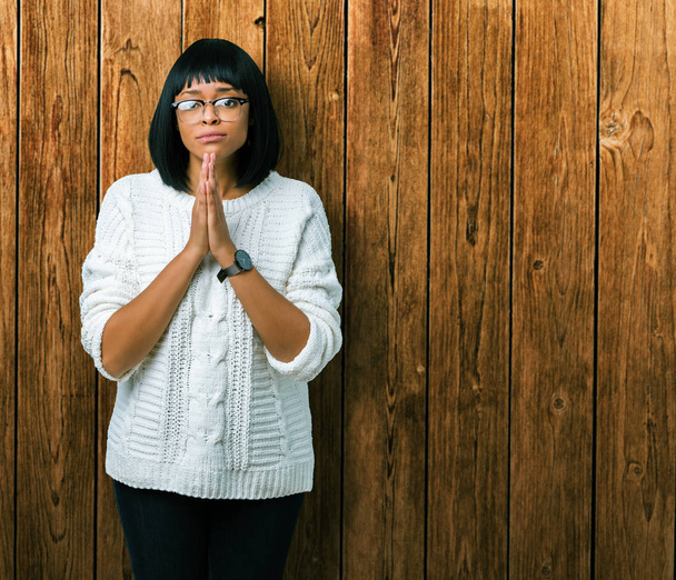 Linda jovem afro-americana vestindo óculos sobre fundo isolado orando com as mãos juntas pedindo perdão sorrindo confiante
. - Foto, Imagem