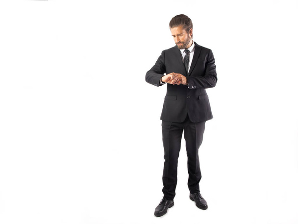 knappe jonge zakenman in zwart pak kijken naar polshorloge geïsoleerd op wit - Foto, afbeelding