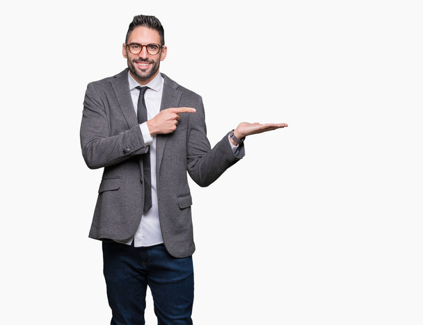 Young handsome business man over isolated background amazed and smiling to the camera while presenting with hand and pointing with finger. - Photo, Image
