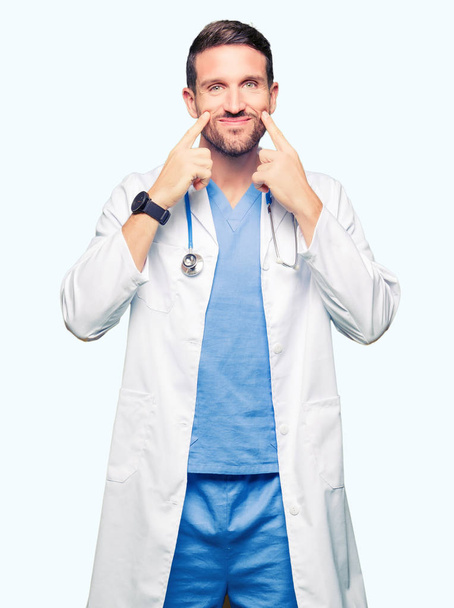 Handsome doctor man wearing medical uniform over isolated background Smiling with open mouth, fingers pointing and forcing cheerful smile - Foto, immagini
