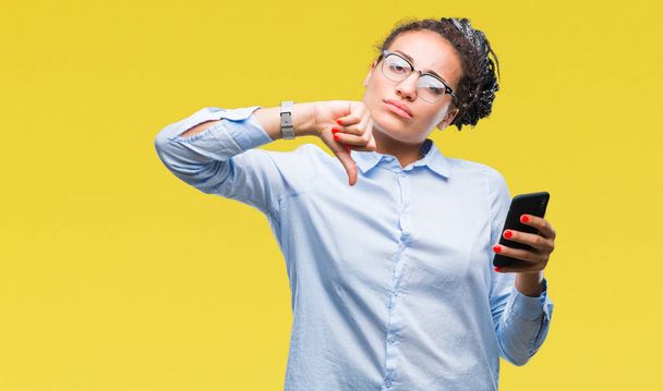 Young braided hair african american business girl using smartphone over isolated background with angry face, negative sign showing dislike with thumbs down, rejection concept - Fotoğraf, Görsel