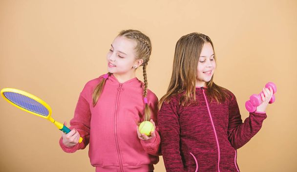 Friends ready for training. Ways to help kids find sport they enjoy. Girls cute kids with sport equipment dumbbells and tennis racket. We love sport. Child might excel in completely different sport - Photo, Image
