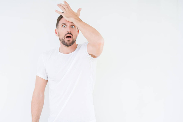 Young handsome man wearing casual white t-shirt over isolated background surprised with hand on head for mistake, remember error. Forgot, bad memory concept. - Photo, Image