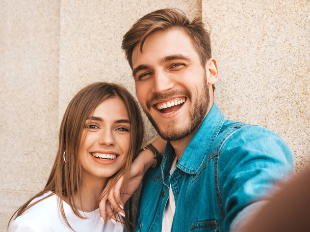 Smiling beautiful girl and her handsome boyfriend in casual summer clothes. Happy family taking selfie self portrait of themselves on smartphone camera. Having fun on the street background  - Photo, image