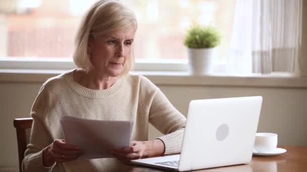 Elderly stressed woman holding bills use laptop check online payments - Imágenes, Vídeo