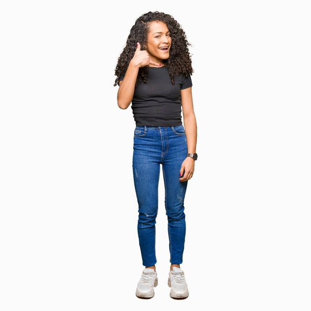 Young beautiful woman with curly hair smiling doing phone gesture with hand and fingers like talking on the telephone. Communicating concepts. - Photo, Image