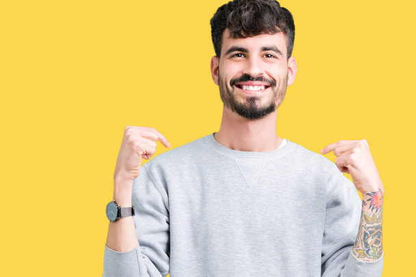 Jonge knappe man dragen sweatshirt over geïsoleerde achtergrond op zoek vertrouwen met glimlach op het gezicht, wijzen zichzelf met de vingers trots en blij. - Foto, afbeelding