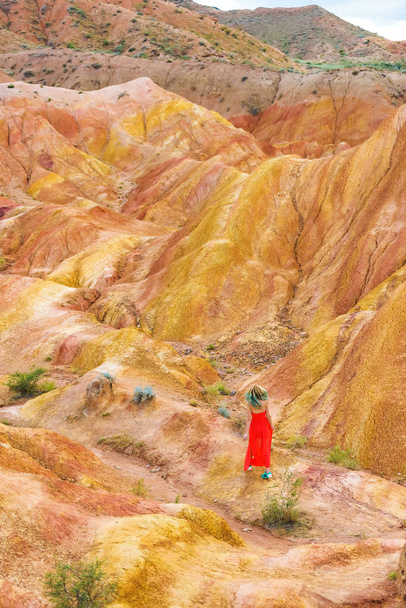 Canyon Tale en Kirguistán. Una chica vestida de rojo contra las colinas de arena. Naturaleza en el área del lago Issyk-Kul
. - Foto, imagen