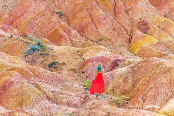 キルギスのキャニオン物語。砂の丘に対して赤いドレスを着た少女。イシククル湖周辺の自然. - 写真・画像