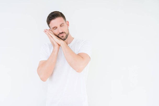Young handsome man wearing casual white t-shirt over isolated background sleeping tired dreaming and posing with hands together while smiling with closed eyes. - Foto, afbeelding