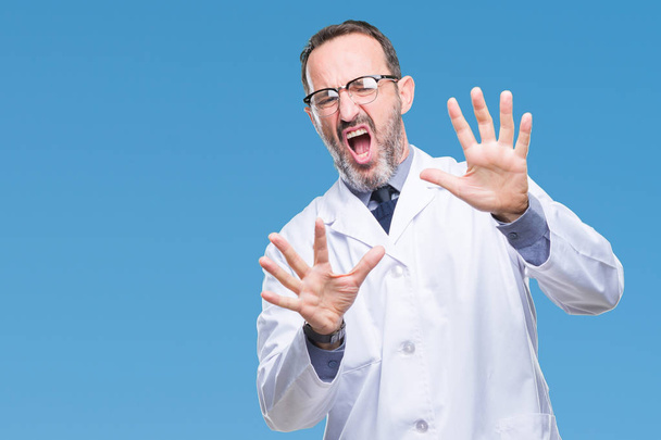 Middle age senior hoary professional man wearing white coat over isolated background afraid and terrified with fear expression stop gesture with hands, shouting in shock. Panic concept. - Fotó, kép