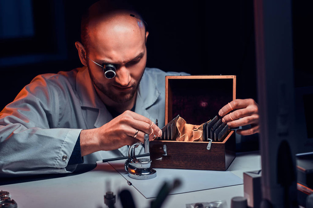 Focused man is working at his workshop with monocle and other tools repairing old watches - Photo, Image