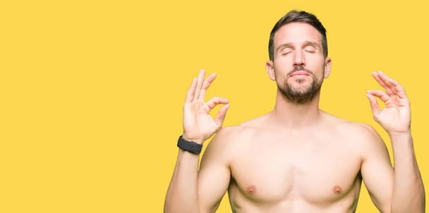Knappe shirtless man tonen naakt borst ontspannen en glimlachen met ogen gesloten doen meditatie gebaar met de vingers. Yoga concept. - Foto, afbeelding