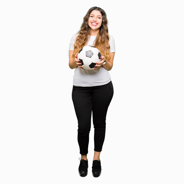 Jonge volwassen vrouw houdt van voetbal voetbal met een blij gezicht permanent en lachend met een vertrouwen glimlach weergeven tanden - Foto, afbeelding