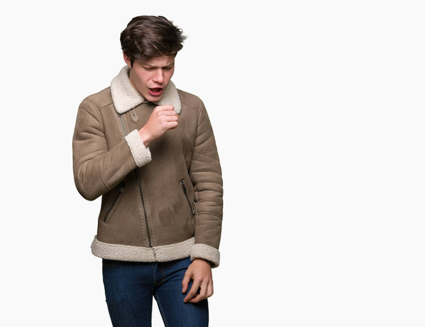 Jonge knappe man dragen winterjas over geïsoleerd achtergrond gevoel onwel en hoesten als symptoom voor koude of bronchitis. Gezondheidszorg concept. - Foto, afbeelding